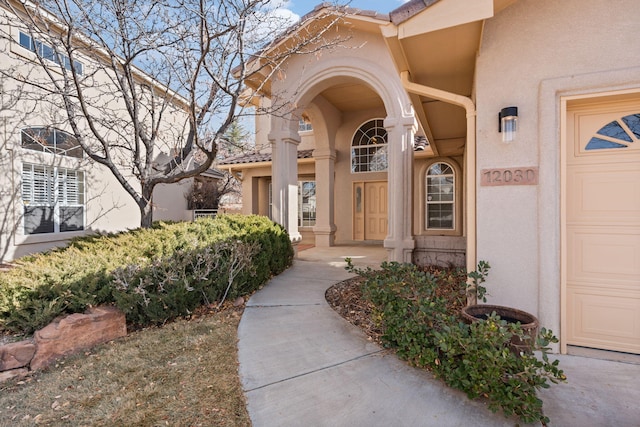 entrance to property with a tiled roof, an attached garage, and stucco siding