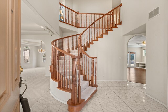 stairway featuring arched walkways, visible vents, crown molding, and a high ceiling