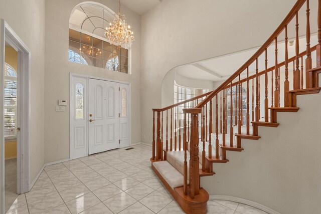 tiled foyer entrance featuring a notable chandelier, a towering ceiling, baseboards, and stairs