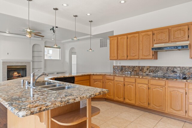 kitchen with black electric stovetop, stone countertops, a sink, a tile fireplace, and under cabinet range hood