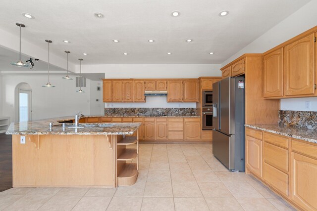 kitchen featuring arched walkways, stainless steel appliances, light stone counters, and under cabinet range hood