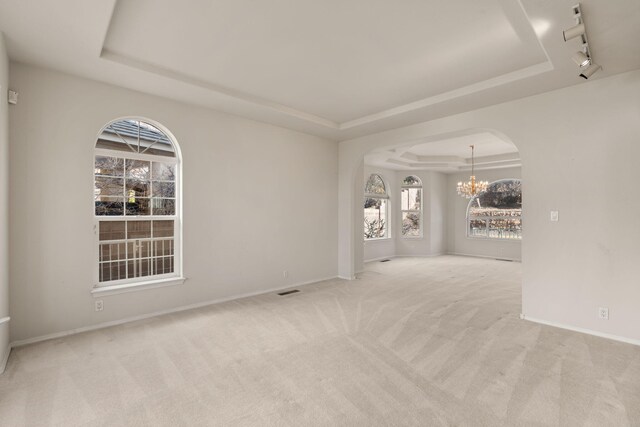 empty room with arched walkways, a raised ceiling, rail lighting, carpet flooring, and a notable chandelier