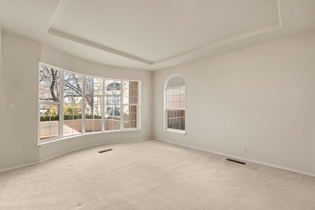 carpeted empty room with a tray ceiling and visible vents