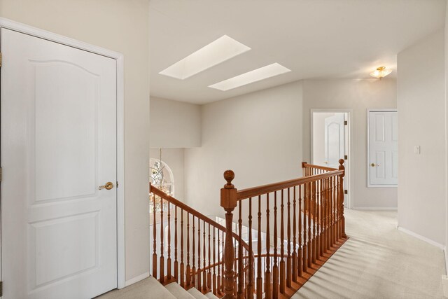 hallway featuring carpet, a skylight, an upstairs landing, and baseboards