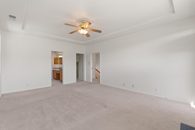 interior space featuring light carpet, visible vents, baseboards, a raised ceiling, and ensuite bath