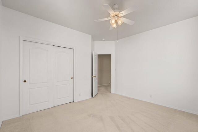 unfurnished bedroom featuring a closet, light colored carpet, ceiling fan, and baseboards