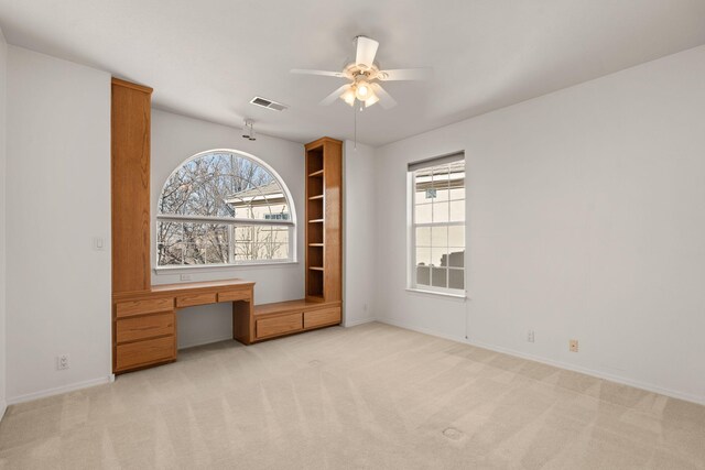 unfurnished bedroom with light carpet, a ceiling fan, visible vents, baseboards, and built in desk