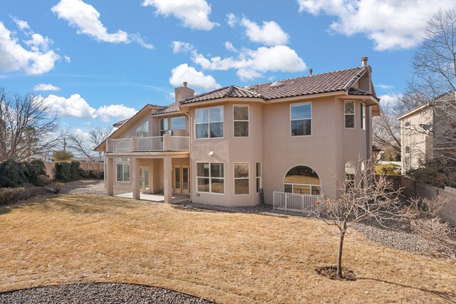 rear view of property with a balcony, a chimney, fence, a patio area, and stucco siding