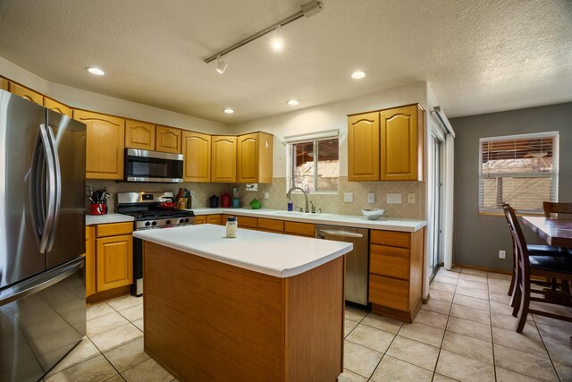 kitchen featuring sink, light tile patterned floors, stainless steel appliances, a kitchen island, and decorative backsplash