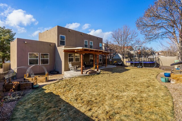 back of house with a fire pit, a yard, a trampoline, and a patio area