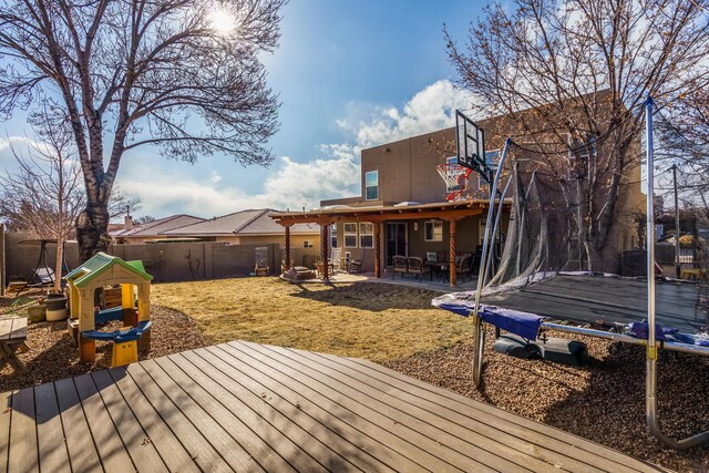 deck with an outdoor fire pit, a playground, and a trampoline