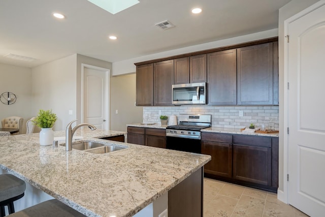 kitchen featuring dark brown cabinetry, sink, a center island with sink, and appliances with stainless steel finishes