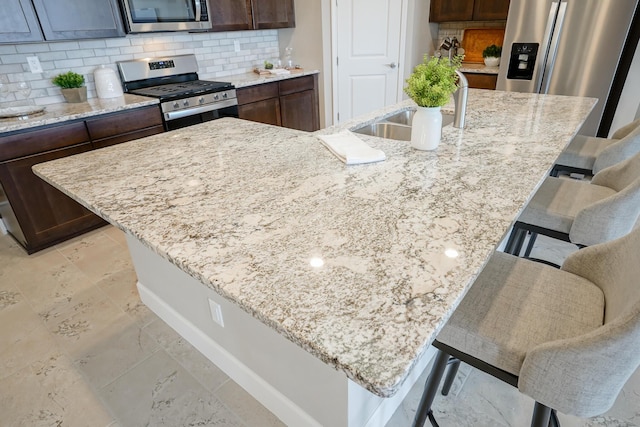 kitchen with a kitchen island with sink, sink, a kitchen breakfast bar, and appliances with stainless steel finishes