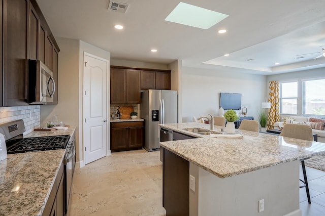 kitchen featuring a breakfast bar area, light stone counters, a skylight, appliances with stainless steel finishes, and a kitchen island with sink