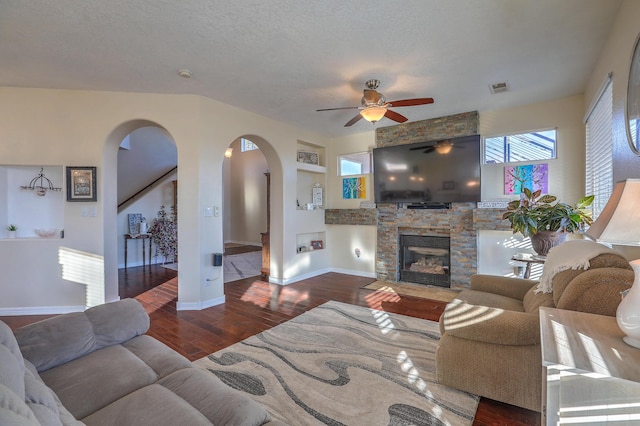 living room featuring dark hardwood / wood-style flooring, ceiling fan, a stone fireplace, and a textured ceiling