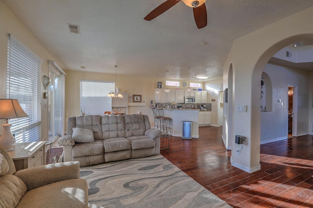 living room featuring dark hardwood / wood-style floors, ceiling fan with notable chandelier, and a textured ceiling