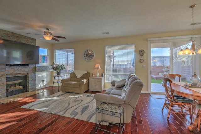 living room featuring dark hardwood / wood-style floors, ceiling fan with notable chandelier, a textured ceiling, and a fireplace