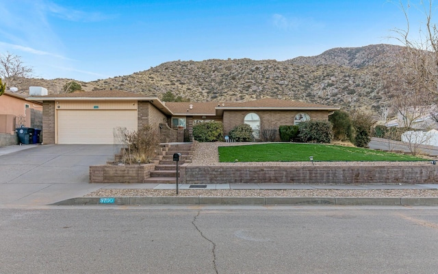 view of front of home featuring brick siding, concrete driveway, an attached garage, a mountain view, and a front lawn