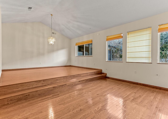 unfurnished room featuring hardwood / wood-style flooring, lofted ceiling, and a chandelier