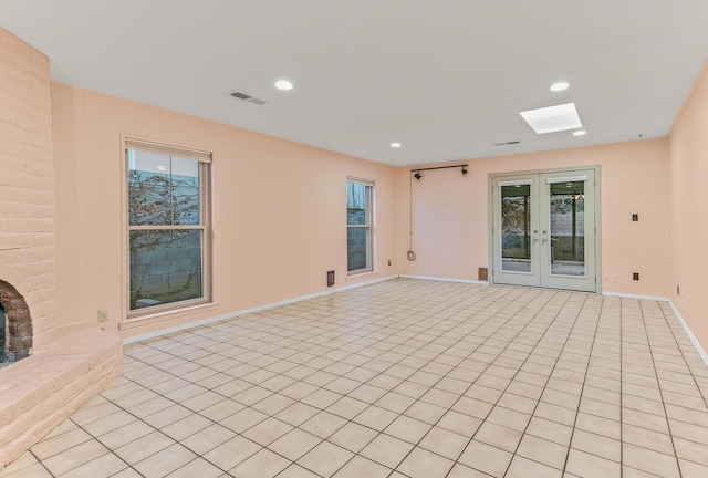 empty room with french doors, a brick fireplace, a healthy amount of sunlight, and a skylight