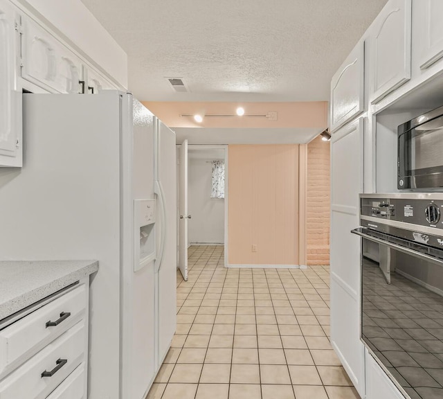 kitchen featuring light tile patterned floors, white cabinetry, white fridge with ice dispenser, a textured ceiling, and oven