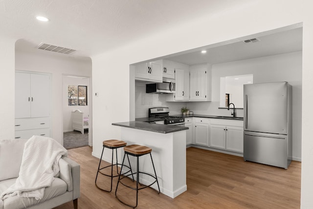 kitchen with sink, light hardwood / wood-style flooring, appliances with stainless steel finishes, white cabinetry, and kitchen peninsula