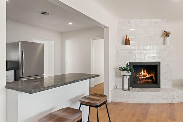 kitchen with a breakfast bar, a fireplace, stainless steel fridge, kitchen peninsula, and light hardwood / wood-style flooring