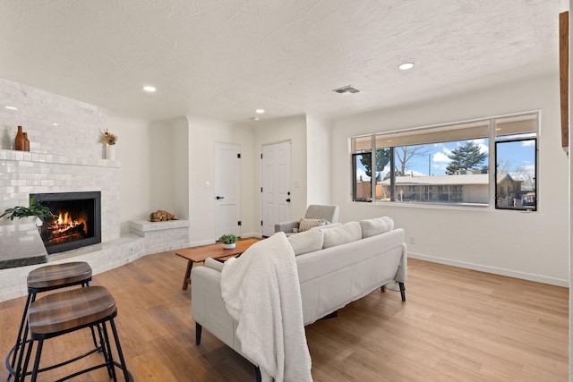 living room featuring a brick fireplace, light hardwood / wood-style floors, and a textured ceiling