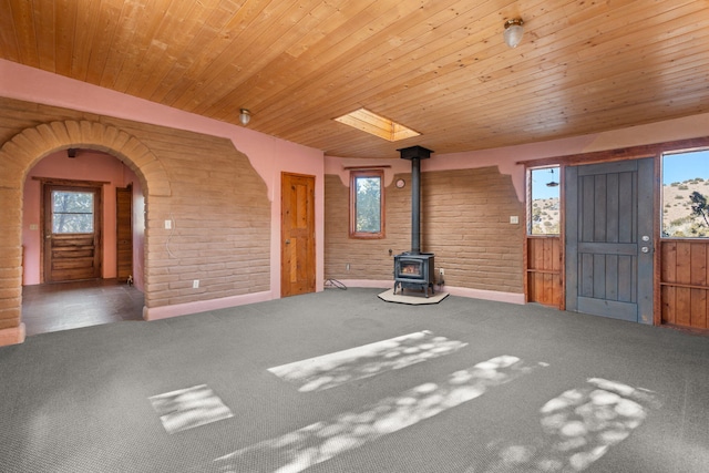 unfurnished living room with a wood stove, a wealth of natural light, and wooden ceiling