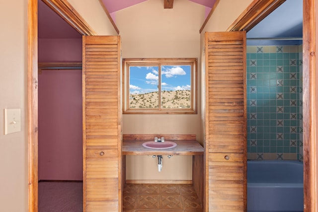 bathroom with vaulted ceiling, tiled shower / bath, and sink