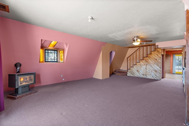 unfurnished living room with a healthy amount of sunlight, a wood stove, ceiling fan, and carpet flooring