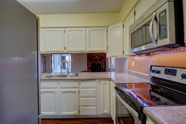 kitchen with stainless steel appliances, a brick fireplace, sink, and white cabinets