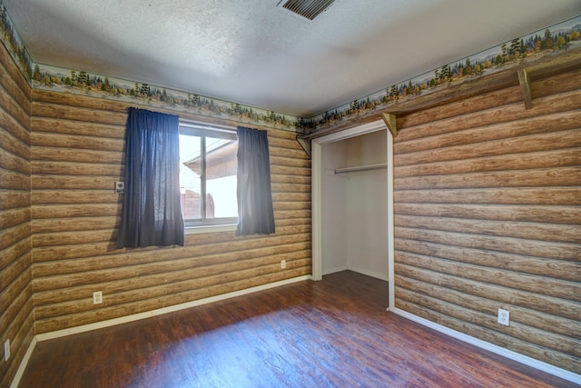 unfurnished bedroom with a closet, dark hardwood / wood-style floors, rustic walls, and a textured ceiling