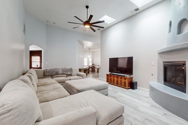 living room featuring a skylight, light hardwood / wood-style flooring, high vaulted ceiling, and ceiling fan