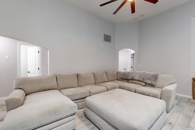 living room featuring ceiling fan, a towering ceiling, and light wood-type flooring