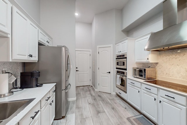 kitchen with white cabinets, decorative backsplash, light hardwood / wood-style floors, and wall chimney exhaust hood