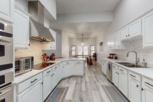 kitchen featuring appliances with stainless steel finishes, white cabinetry, sink, hanging light fixtures, and wall chimney exhaust hood