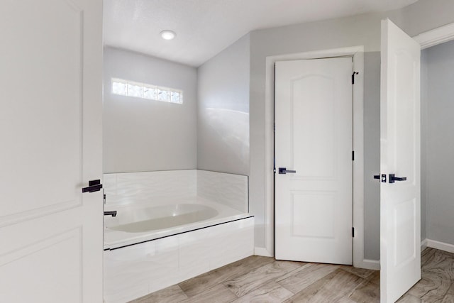 bathroom with a relaxing tiled tub and hardwood / wood-style flooring