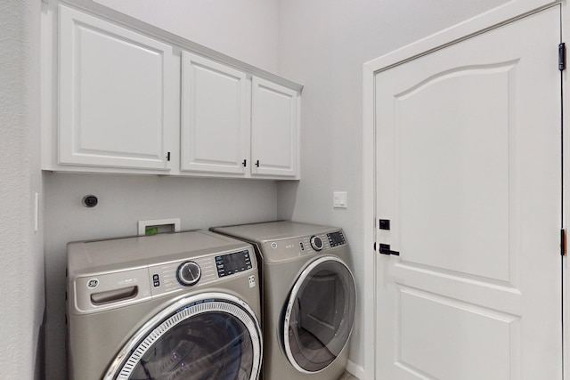 clothes washing area with cabinets and washing machine and clothes dryer