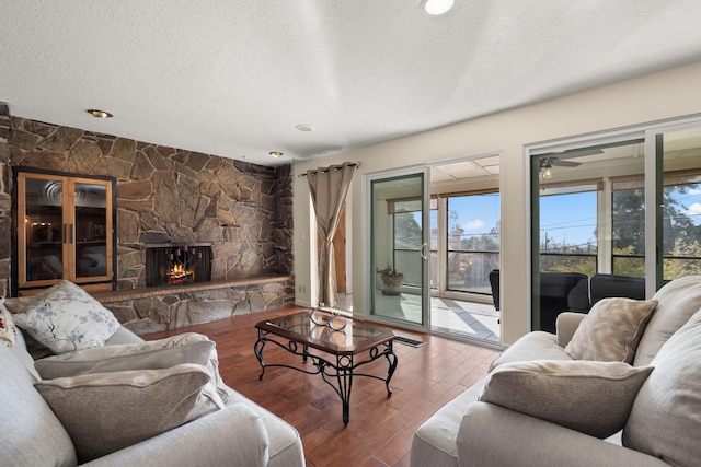 living room featuring hardwood / wood-style flooring, a stone fireplace, and a textured ceiling