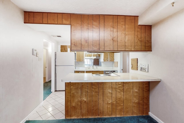 kitchen featuring cooktop, sink, light tile patterned floors, kitchen peninsula, and white fridge