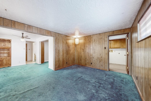 empty room with carpet, a textured ceiling, and wood walls