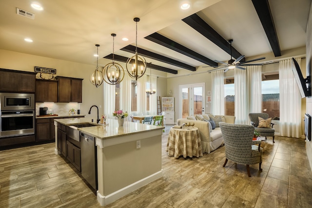 kitchen with appliances with stainless steel finishes, sink, light stone counters, dark brown cabinets, and a center island with sink