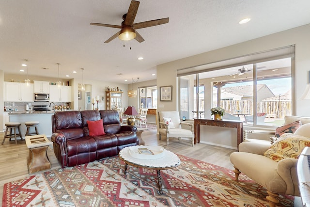 living room with ceiling fan, a textured ceiling, and light wood-type flooring