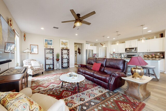 living room featuring sink, a textured ceiling, light hardwood / wood-style flooring, and ceiling fan