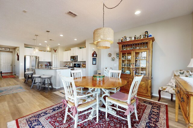 dining room with an inviting chandelier, light hardwood / wood-style floors, and a textured ceiling