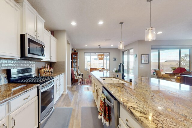 kitchen with pendant lighting, white cabinetry, sink, stainless steel appliances, and light stone countertops