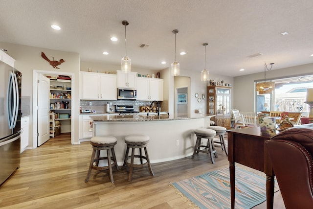 kitchen with decorative light fixtures, an island with sink, white cabinetry, a breakfast bar area, and stainless steel appliances