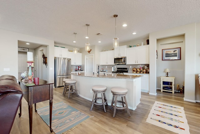 kitchen with decorative light fixtures, a center island with sink, stainless steel appliances, light stone countertops, and white cabinets