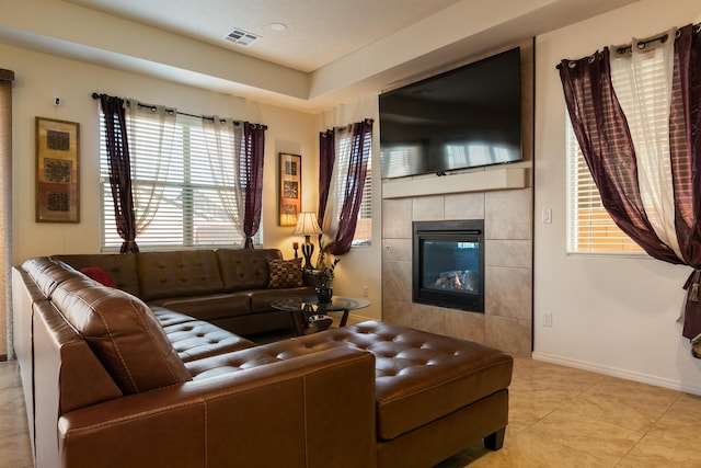 living area with baseboards, visible vents, a tiled fireplace, and light tile patterned floors